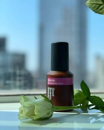 Bottle of 004-Br Skin Brightening Cream with white rose placed in front of it against out of focus background of New York skyline