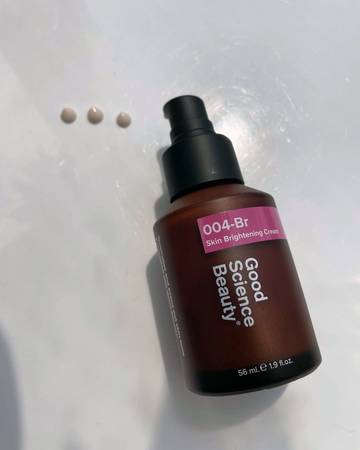 Bottle of 004-Br Skin Brightening Cream on white surface, with three small blobs of dispensed cream beside the  pump